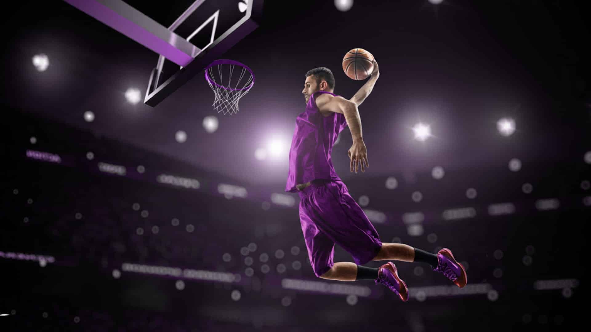 Basketball player in purple uniform mid-air approaching the basket in a packed arena